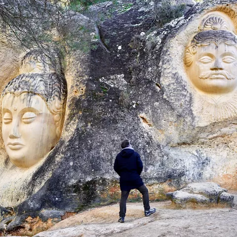 Esculturas de rostros humanos talladas en la pared rocosa.
