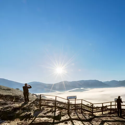 Amanecer sobre montañas con mirador y visitantes.