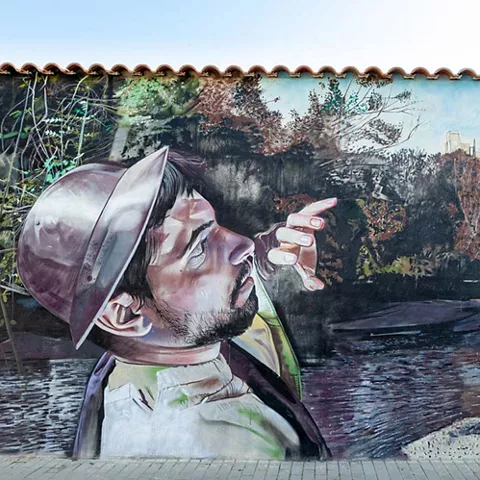 Mural de hombre con casco medieval señalando un castillo junto a un río.