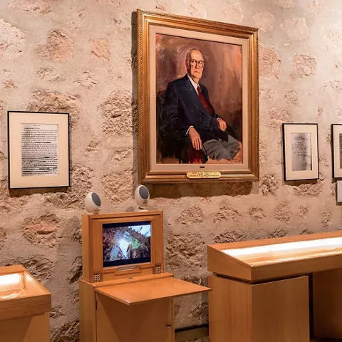 Sala expositiva con retrato y vitrinas iluminadas.