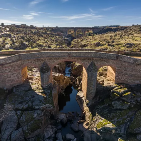 Primer plano elevado de un puente de piedra con tajamares puntiagudos que cruza un río encajonado entre rocas.