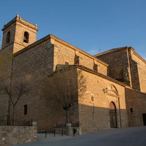 Una iglesia antigua de piedra dorada con un campanario cuadrado bajo un cielo azul despejado.
