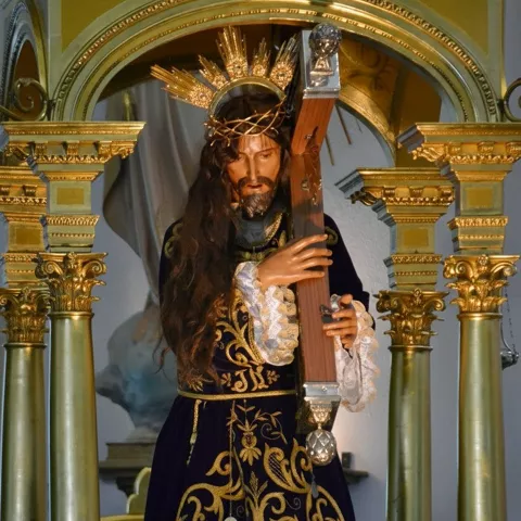 Imagen religiosa vestida de morado entre columnas doradas.