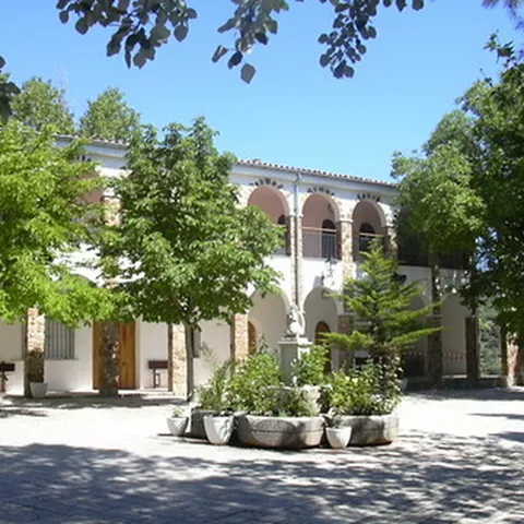 Patio ajardinado con edificio blanco de arcos y árboles que dan sombra.