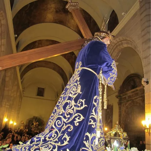 Imagen religiosa con cruz a hombros dentro de una iglesia, vestida con manto bordado azul.