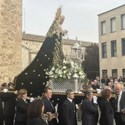 Personas portando un paso con figura velada y arreglo floral, rodeadas de público en la calle.