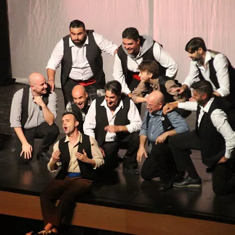 Grupo de actores masculinos reunidos en escena durante interpretación coral