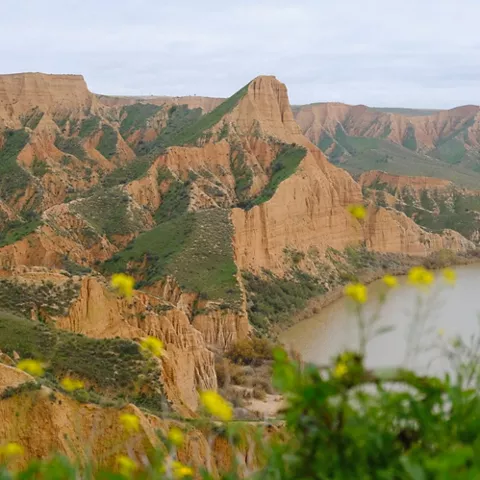Barrancos de arcilla rojiza con vegetación verde junto a un embalse.