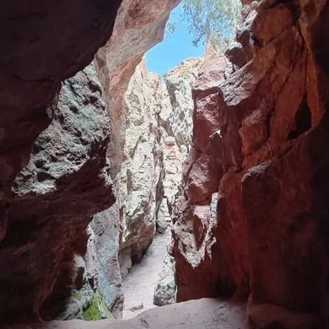 Sendero en desfiladero de roca rojiza con cielo visible al fondo.