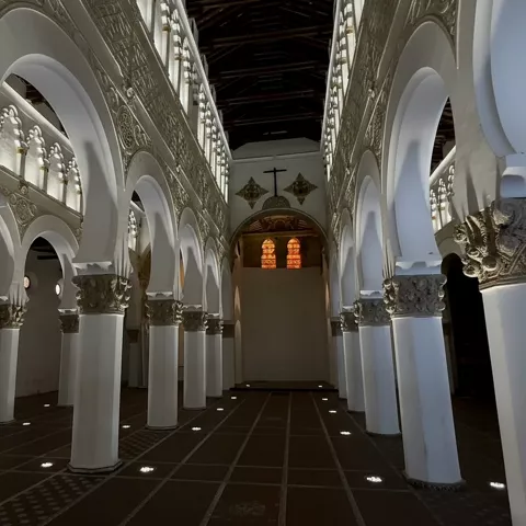 Vista central de sala con columnas alineadas y ventanales al fondo.