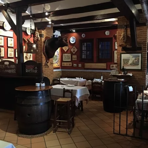 Comedor rústico con mesas vestidas, barriles altos y decoración taurina.