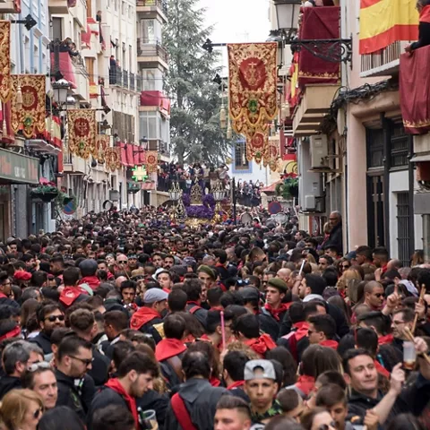 alle estrecha abarrotada con estandartes colgantes y una procesión al fondo.