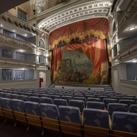 Patio de butacas con asientos azules frente a escenario decorado.