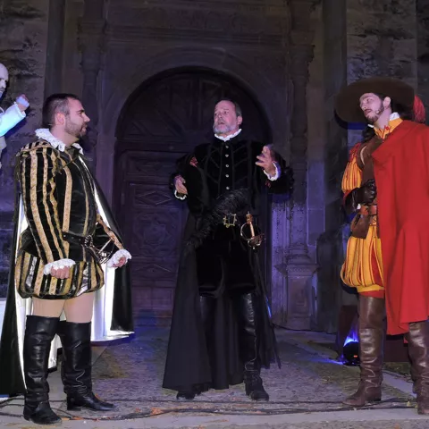 Actores con trajes de época ante portada antigua.