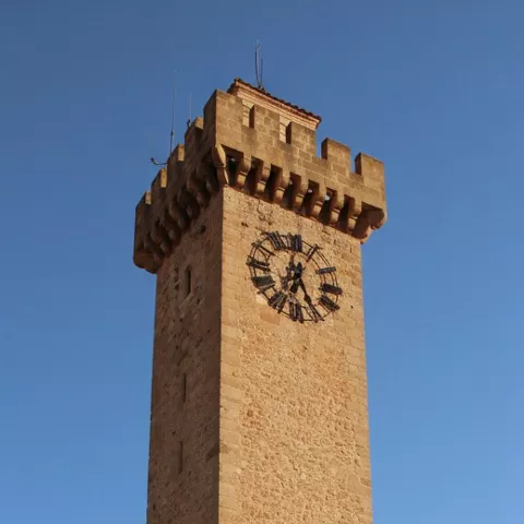 Detalle de torre almenada con reloj sobre fondo azul.