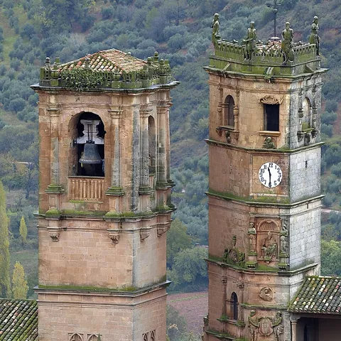 Dos torres históricas de piedra con campana y reloj, cubiertas de vegetación en un entorno natural.