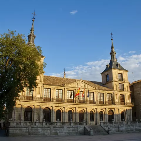Un edificio histórico de estilo clásico con una balconada corrida, arcos en la planta baja y dos torres simétricas con agujas metálicas.