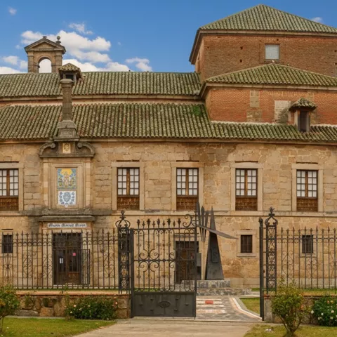 Un edificio histórico de piedra y ladrillo, con múltiples ventanas y un pequeño campanario