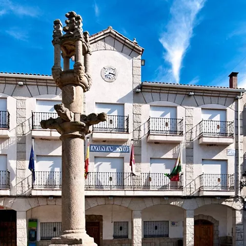 Columna de piedra monumental en una plaza con edificio institucional al fondo.