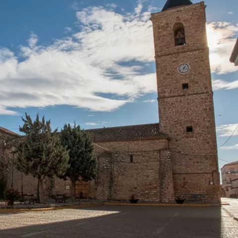 Iglesia parroquial de Villavaliente con torre campanario y plaza con fuente en primer plano.