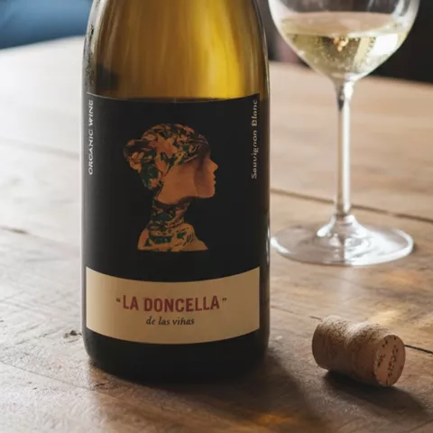 Botella de vino blanco junto a copa en mesa interior.