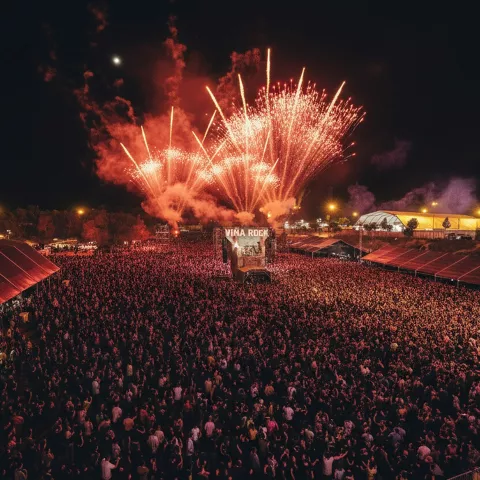 Panorama nocturno de un recinto de conciertos lleno de gente con fuegos artificiales sobre el escenario.
