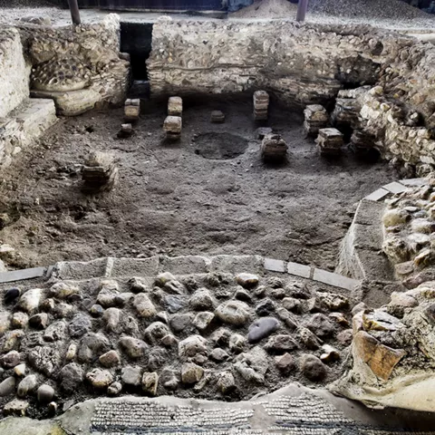 Restos arqueológicos de una estructura circular con muros de piedra y bases de columnas.