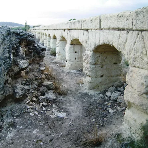 Arcos de piedra antiguos junto a ruinas y terreno seco.