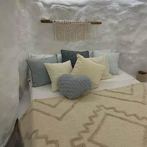 Cama con cojines y manta en habitación excavada en roca blanca.