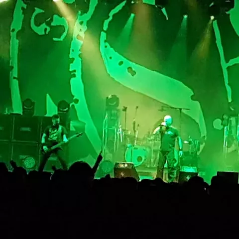 Concierto en directo con banda sobre el escenario iluminado en verde.