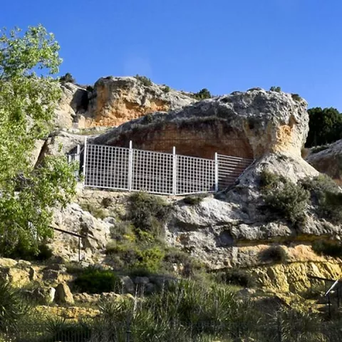 Abrigo rocoso con cerramiento metálico integrado en la pared.