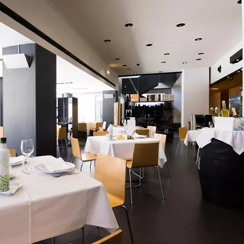 Comedor elegante con mesas vestidas, sillas de madera y ambiente luminoso.