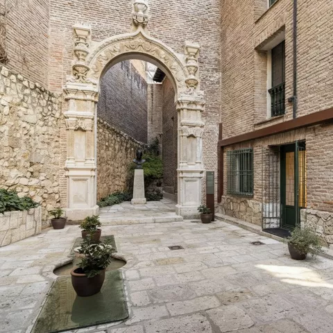 Patio empedrado con arco ornamental de piedra y macetas decorativas.