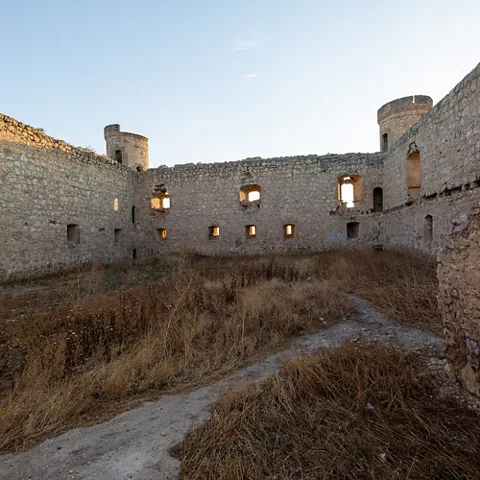 Patio interior de fortaleza con muros de piedra y vegetación seca.