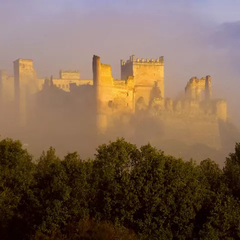 Fortaleza medieval emergiendo entre niebla al amanecer