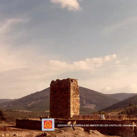 Torre medieval aislada sobre terreno abierto con sierras al fondo.