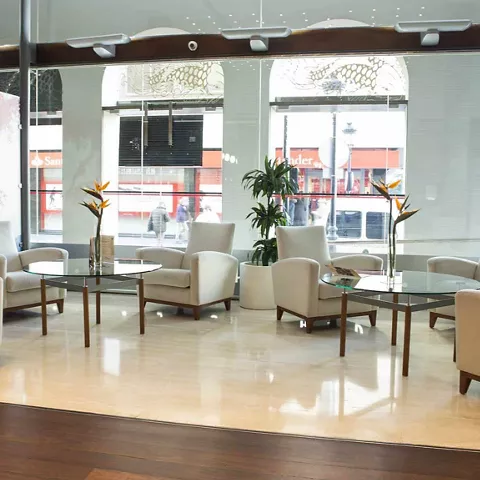 Salón interior luminoso con sillones claros, mesas bajas y grandes ventanales.