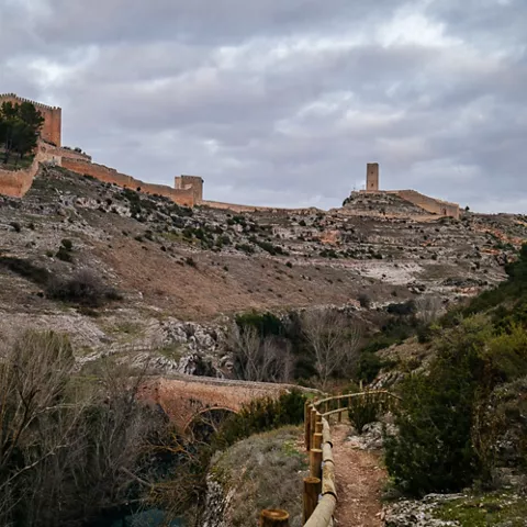 Sendero de tierra junto a un valle rocoso con murallas antiguas en lo alto