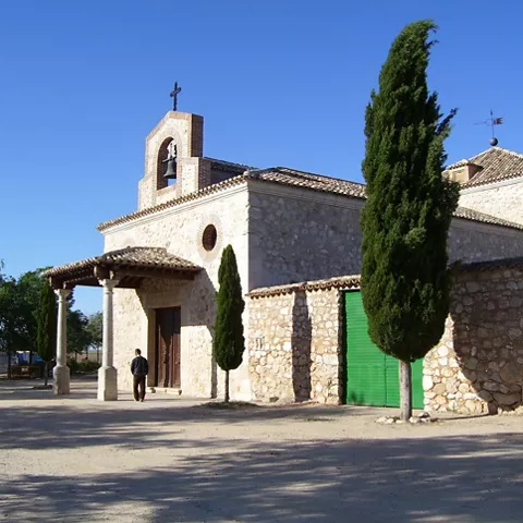 Iglesia de piedra con pórtico y cipreses junto a una explanada