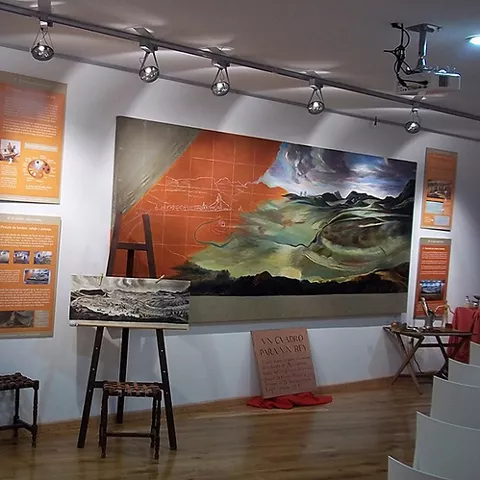 Sala expositiva con paneles informativos, pantalla audiovisual y una gran pintura mural.