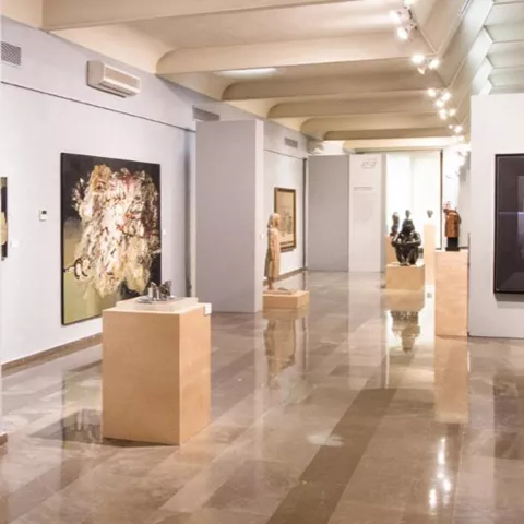 Galería de arte con pinturas y esculturas distribuidas en un recorrido lineal.