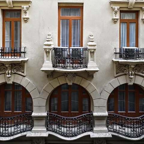Fachada interior con balcones curvos de hierro y ventanas enmarcadas por molduras decorativas.
