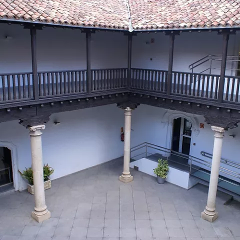 Patio interior con columnas de piedra, galerías de madera y suelo empedrado.