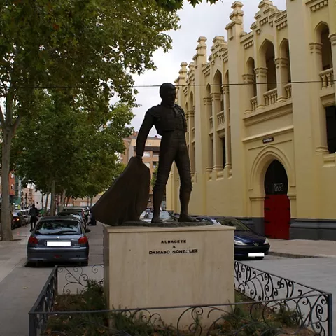 Escultura de torero sobre pedestal frente a edificio histórico.