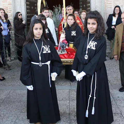Salida procesional diurna con jóvenes portando palmas y figura religiosa.