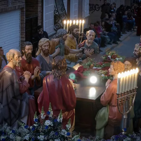Escena nocturna de un paso procesional con figuras alrededor de una mesa iluminada por velas.
