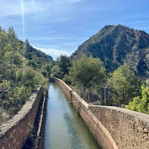 Canal de agua entre muros de piedra rodeado de vegetación y montañas