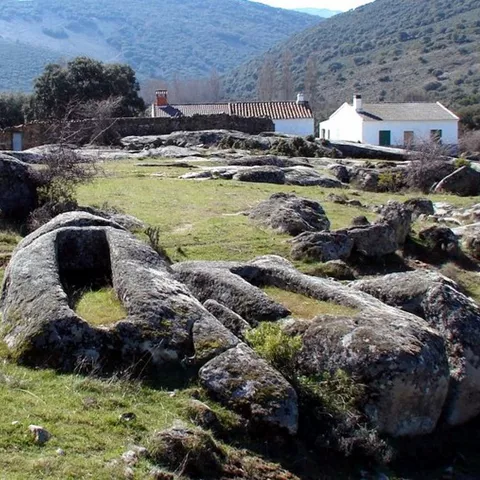 Sepulturas talladas en roca entre praderas y viviendas rurales.