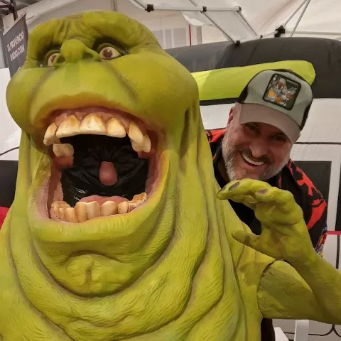 Figura decorativa de personaje verde junto a expositor en feria temática.