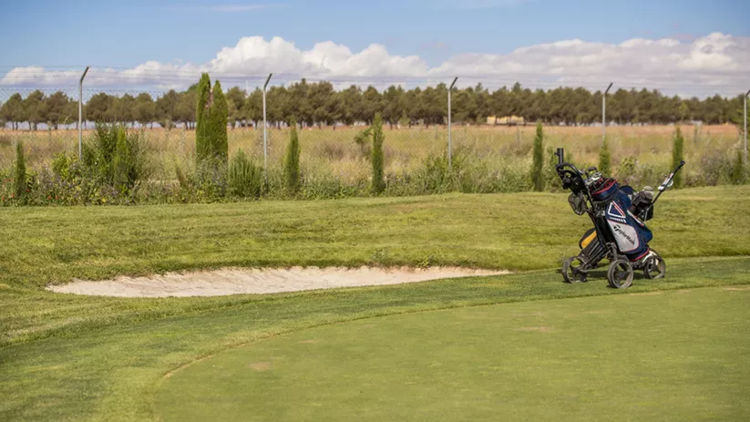 Green de golf con carrito y bunker de arena al fondo